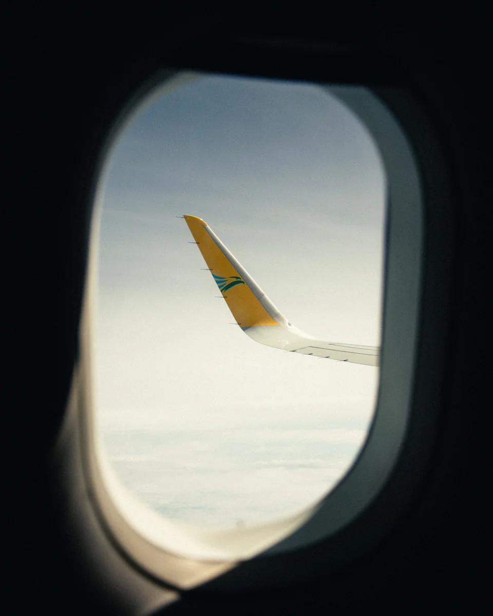 Yellow-tipped aircraft wing seen through a cabin window above the clouds