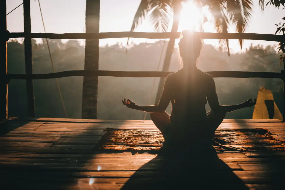 Woman meditating on a wooden deck above the jungle at sunrise
