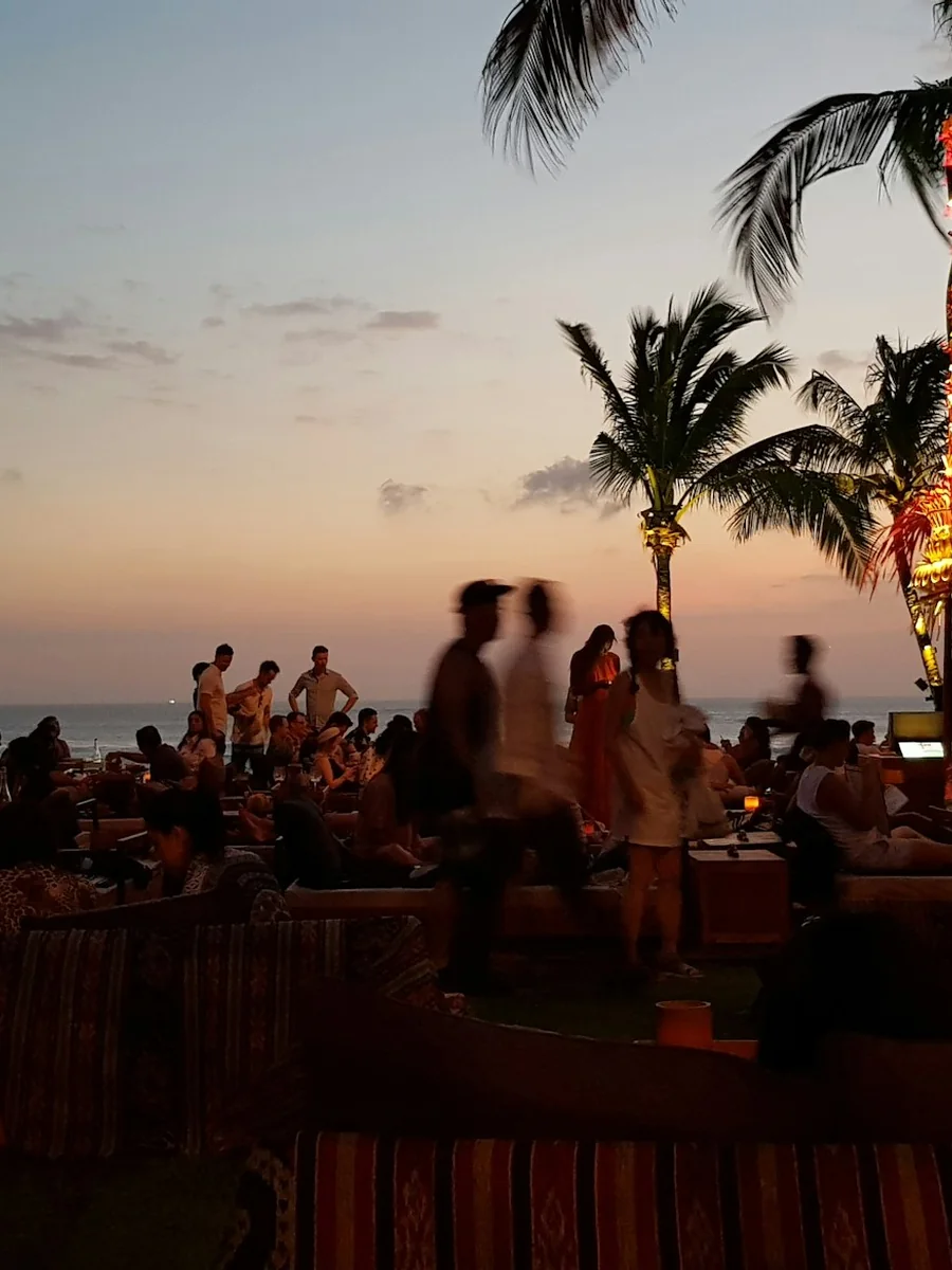 Crowd gathered on Seminyak Beach at sunset under palm trees