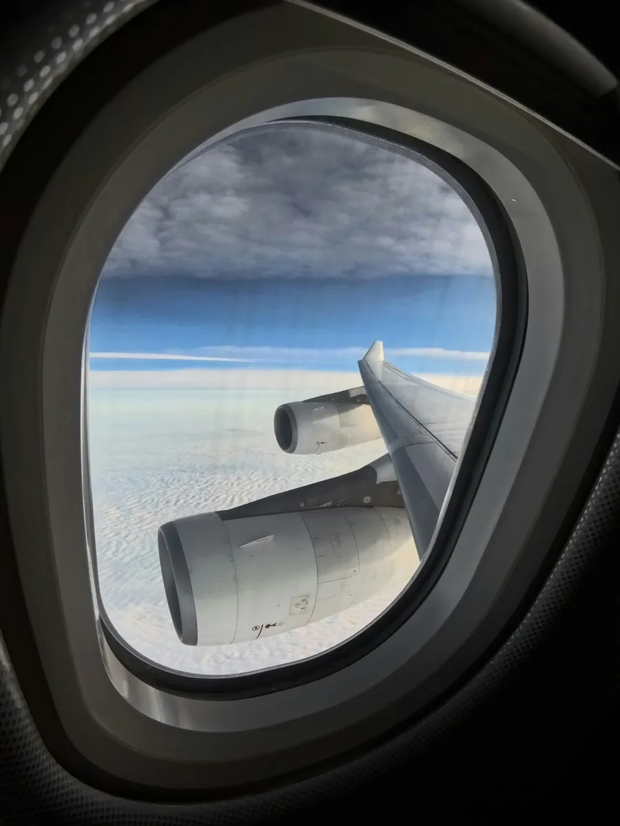 Aircraft wing seen through a cabin window above the clouds