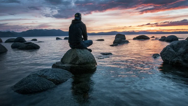 Man sitting quietly on a rock surrounded by water