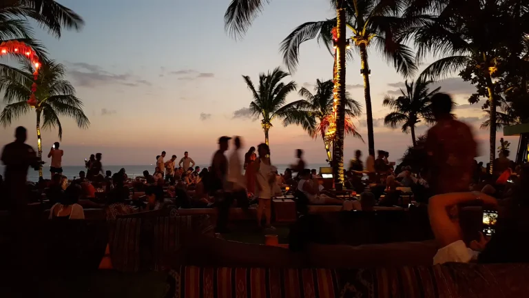 Crowd on a Bali beach at dusk with palm trees and lights