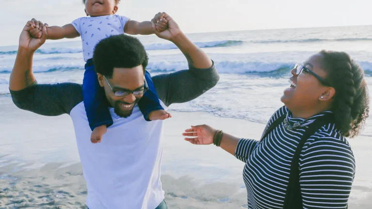 Family on a beach with a man carrying a baby on his shoulders